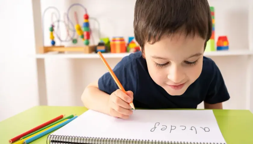 Niño concentrado practicando lectoescritura con lápiz y colores. Aprende el abecedario en su cuaderno.