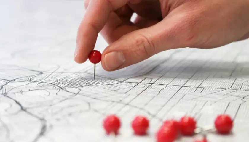 Una mano coloca un alfiler rojo sobre un mapa, marcando puntos clave para planificar rutas de aprendizaje y explorar nuevas posibilidades.