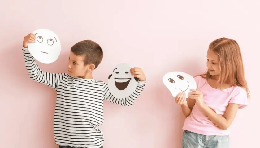 Niños exploran la **educación emocional que es** al sostener máscaras con diferentes expresiones.