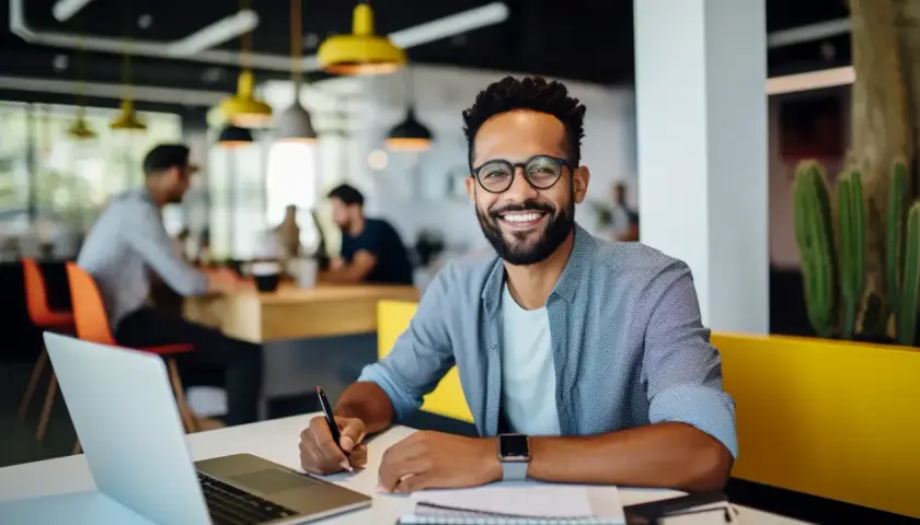 Hombre sonriente trabaja en su portátil, aplicando **técnicas de aprendizaje** en un espacio moderno.