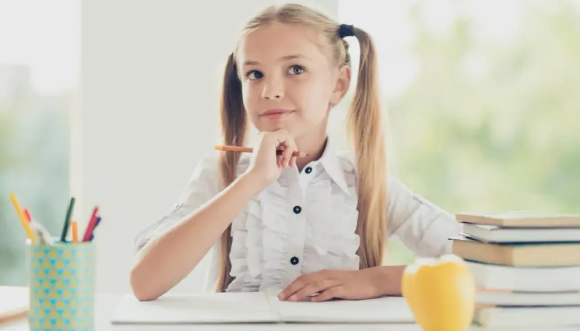 Niña pensativa con lápiz, rodeada de útiles escolares y libros. Ideas para **técnicas de estudio para niños**.
