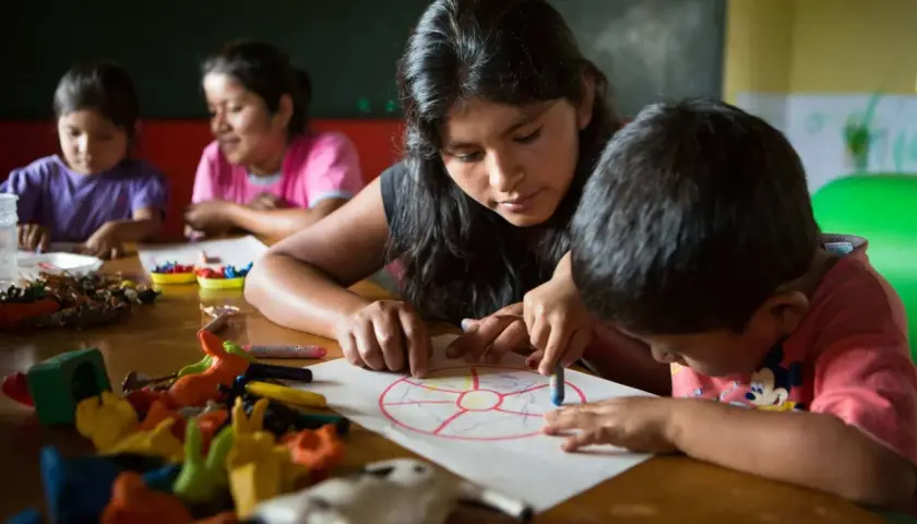 Joven guía a niños en actividad de educación en valores infantil, coloreando un círculo dividido en secciones.