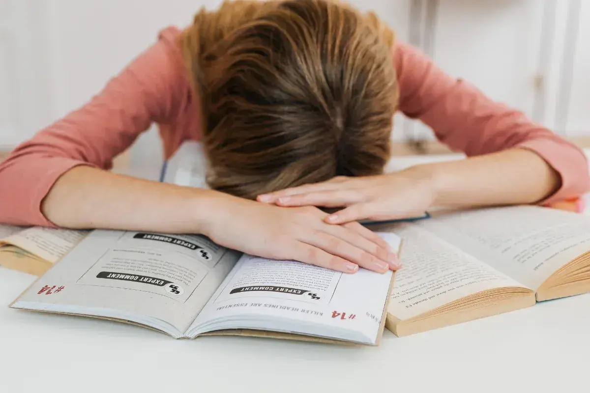 Estudiante agotado sobre libros. Aprende como controlar los nervios antes de un examen y recupera tu energía.