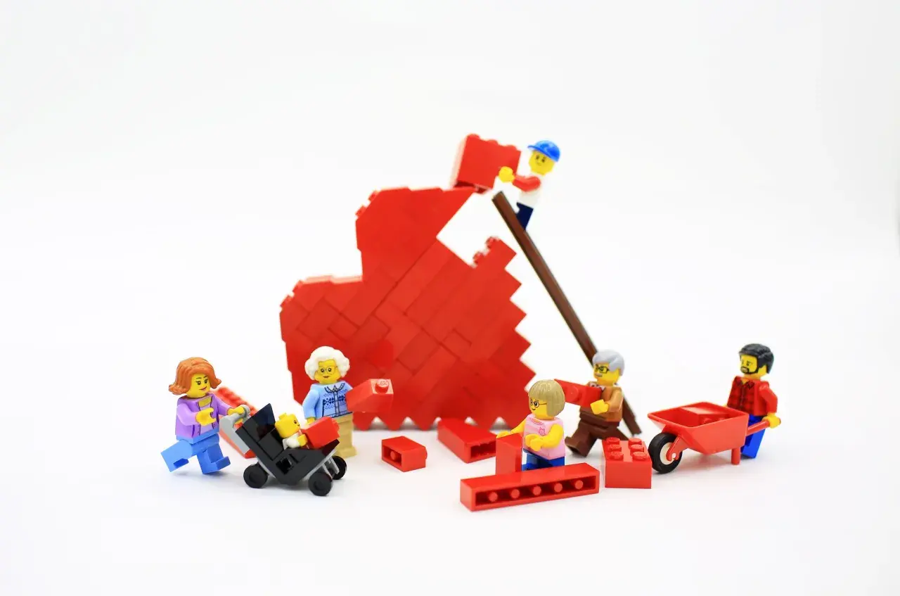 Figuras de Lego construyen un corazón rojo, simbolizando la bisquerra educación emocional y el trabajo en equipo familiar.
