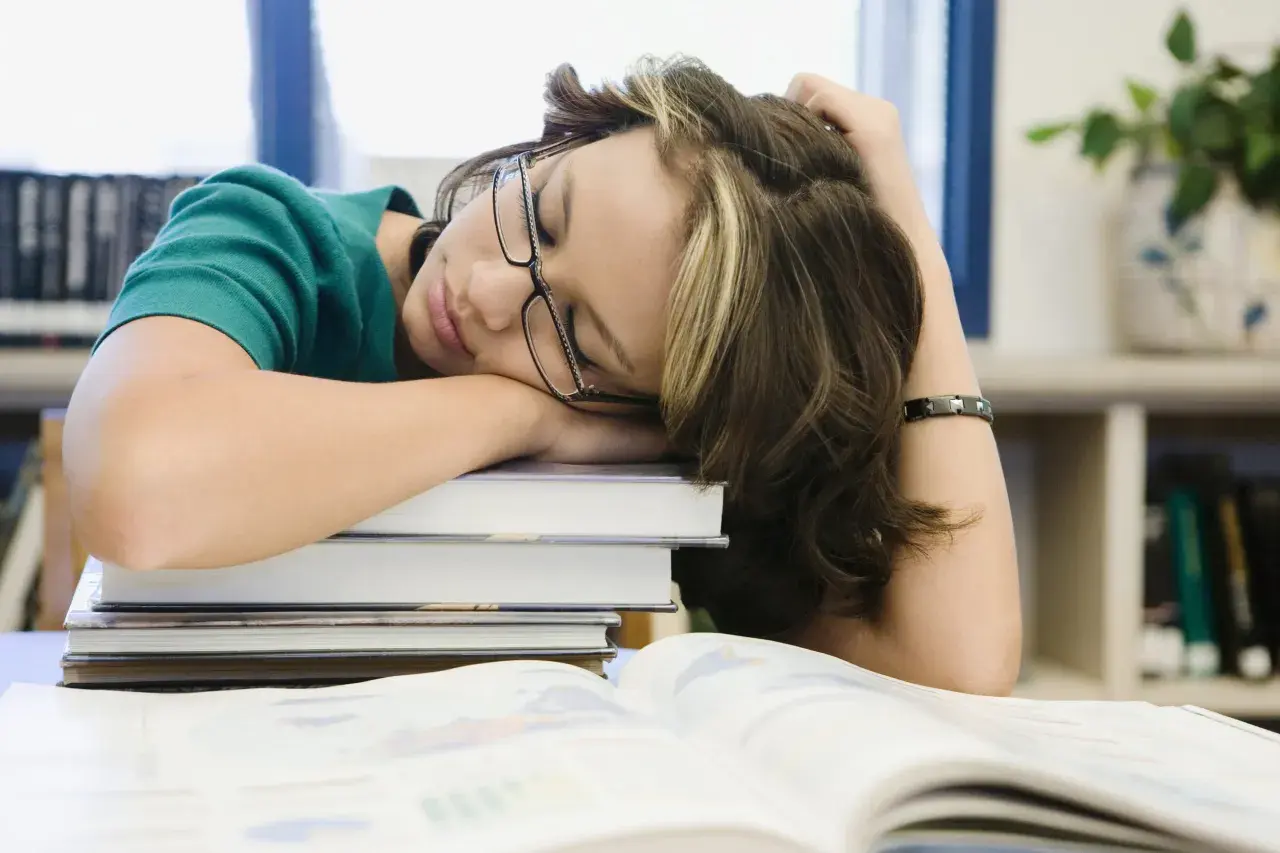 Estudiante dormida sobre libros, buscando cómo tener motivación para seguir estudiando.