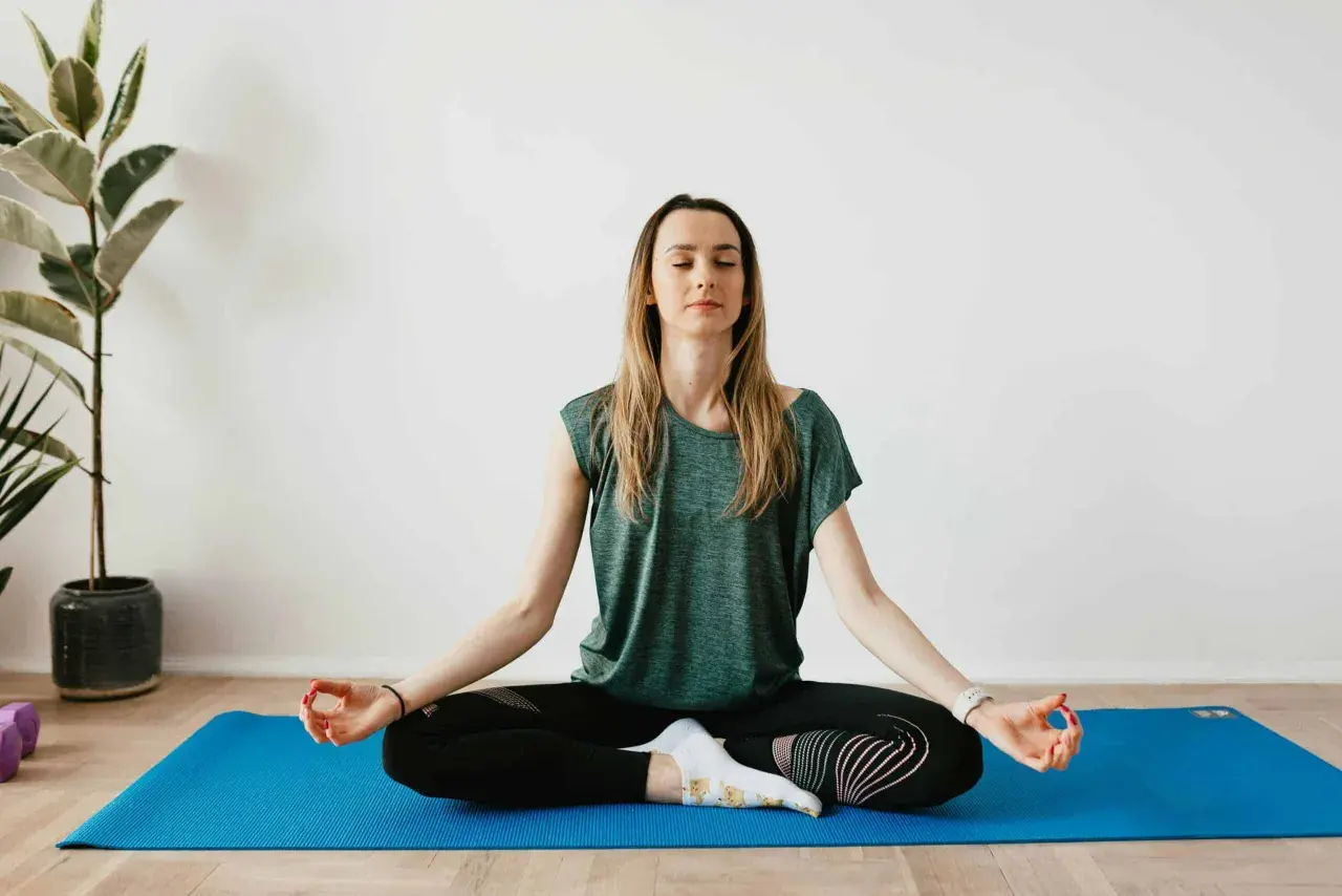 Mujer meditando en postura de loto sobre una esterilla azul. Sus ojos están cerrados, buscando calmar ansiedad y relajar la mente.