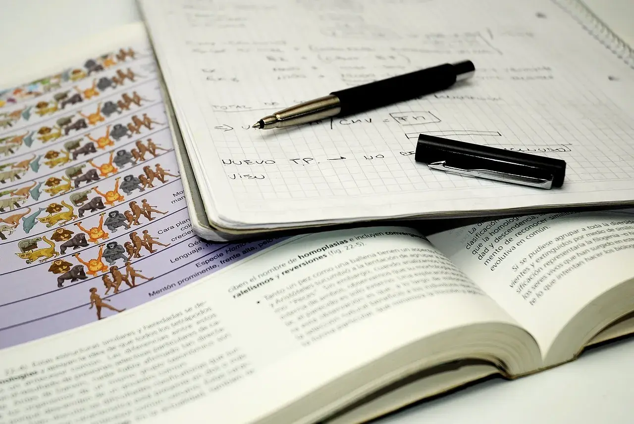 Apuntes para estudiar: cuaderno con notas, bolígrafo, libro abierto y lámina de evolución.