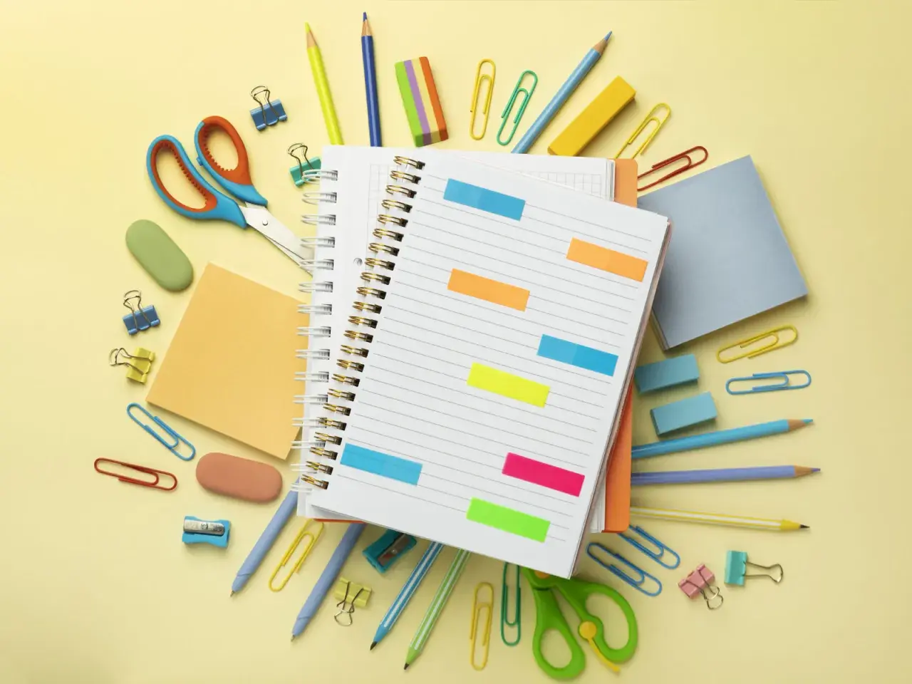 Un cuaderno abierto con notas adhesivas de colores, tijeras, lápices y clips. ¡Todo listo para como organizarme!