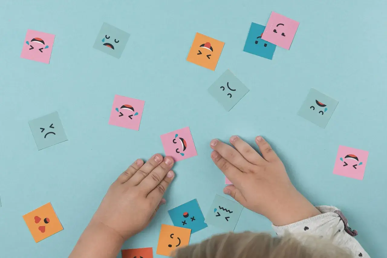 Manos de niño interactuando con tarjetas de emociones, fomentando el aprendizaje emocional.