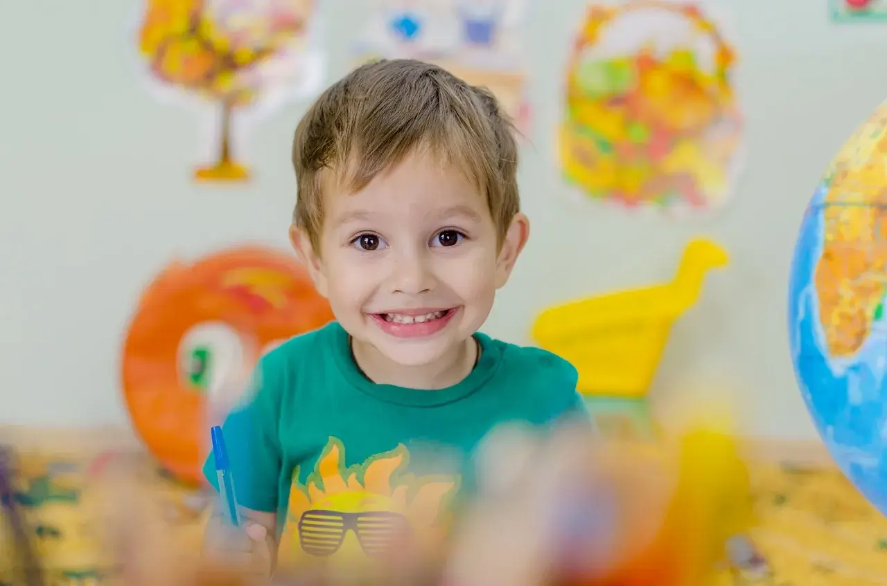 Niño sonriente con camiseta verde, rodeado de materiales educativos que fomentan la autoestima niños.