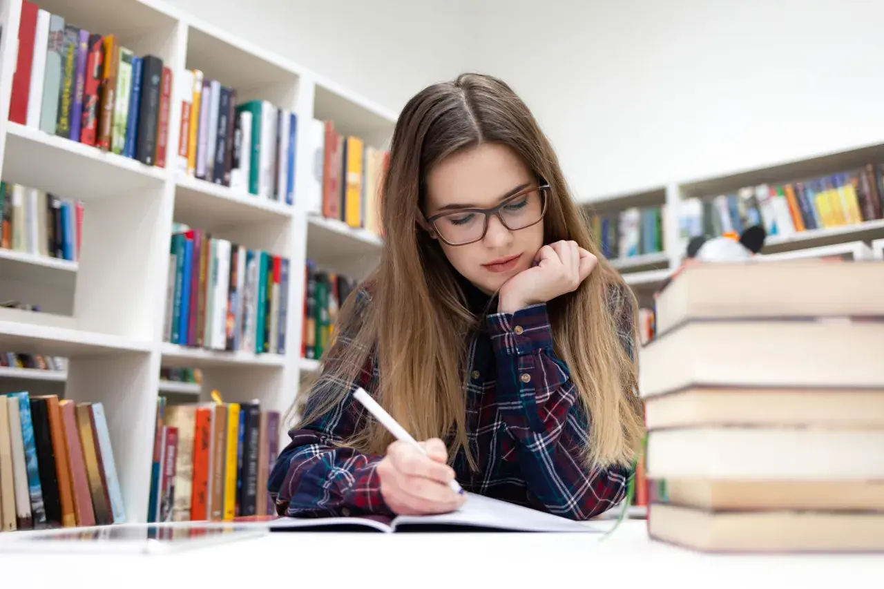 Joven concentrada en su estudio biblioteca en casa, rodeada de estanterías llenas de libros.