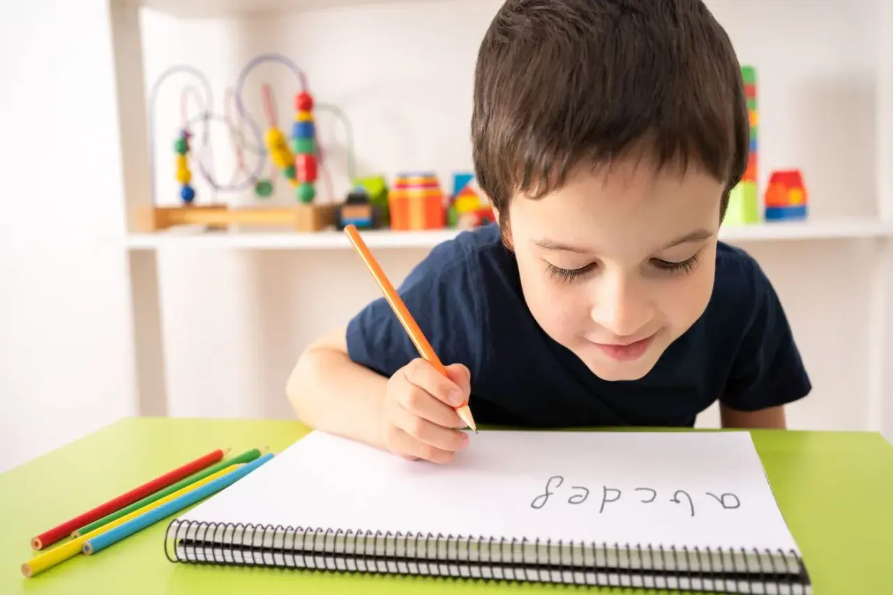 Niño concentrado practicando lectoescritura con lápiz y colores. Aprende el abecedario en su cuaderno.