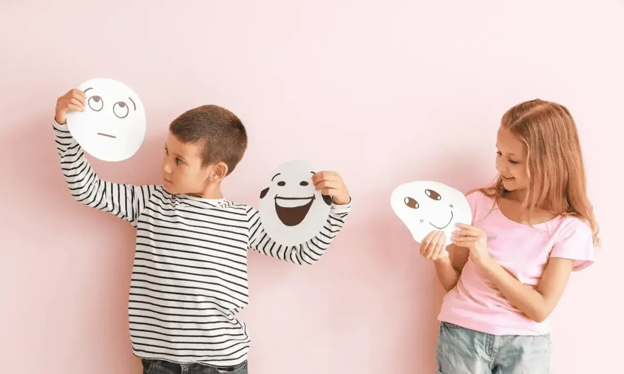 Niños exploran la **educación emocional que es** al sostener máscaras con diferentes expresiones.