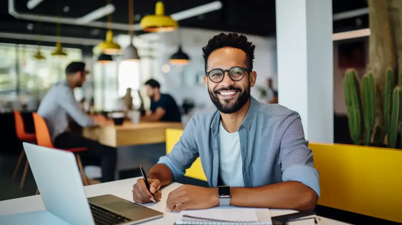 Hombre sonriente trabaja en su portátil, aplicando **técnicas de aprendizaje** en un espacio moderno.