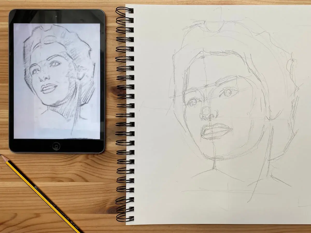 Aprendiendo como dibujar retratos. Boceto a lápiz de un rostro en un cuaderno, con una tablet mostrando el modelo.