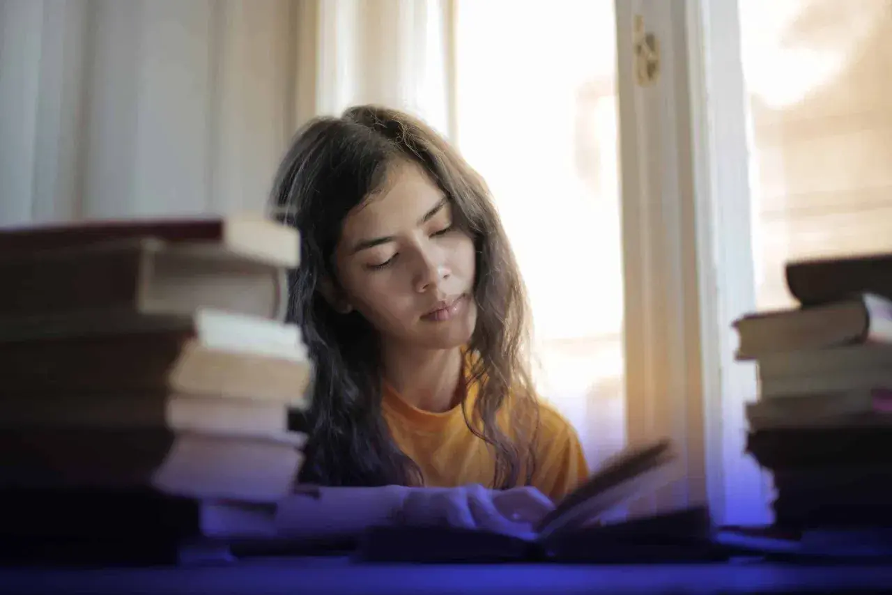 Joven concentrada estudiando, rodeada de libros, buscando técnicas para como memorizar fechas importantes.