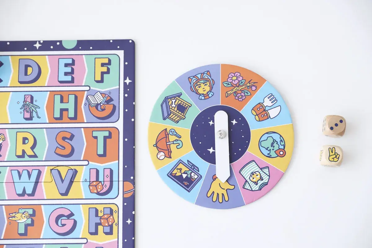 Juego de mesa para lectoescritura infantil con abecedario y ruleta de imágenes. Dados de madera con números y símbolos.