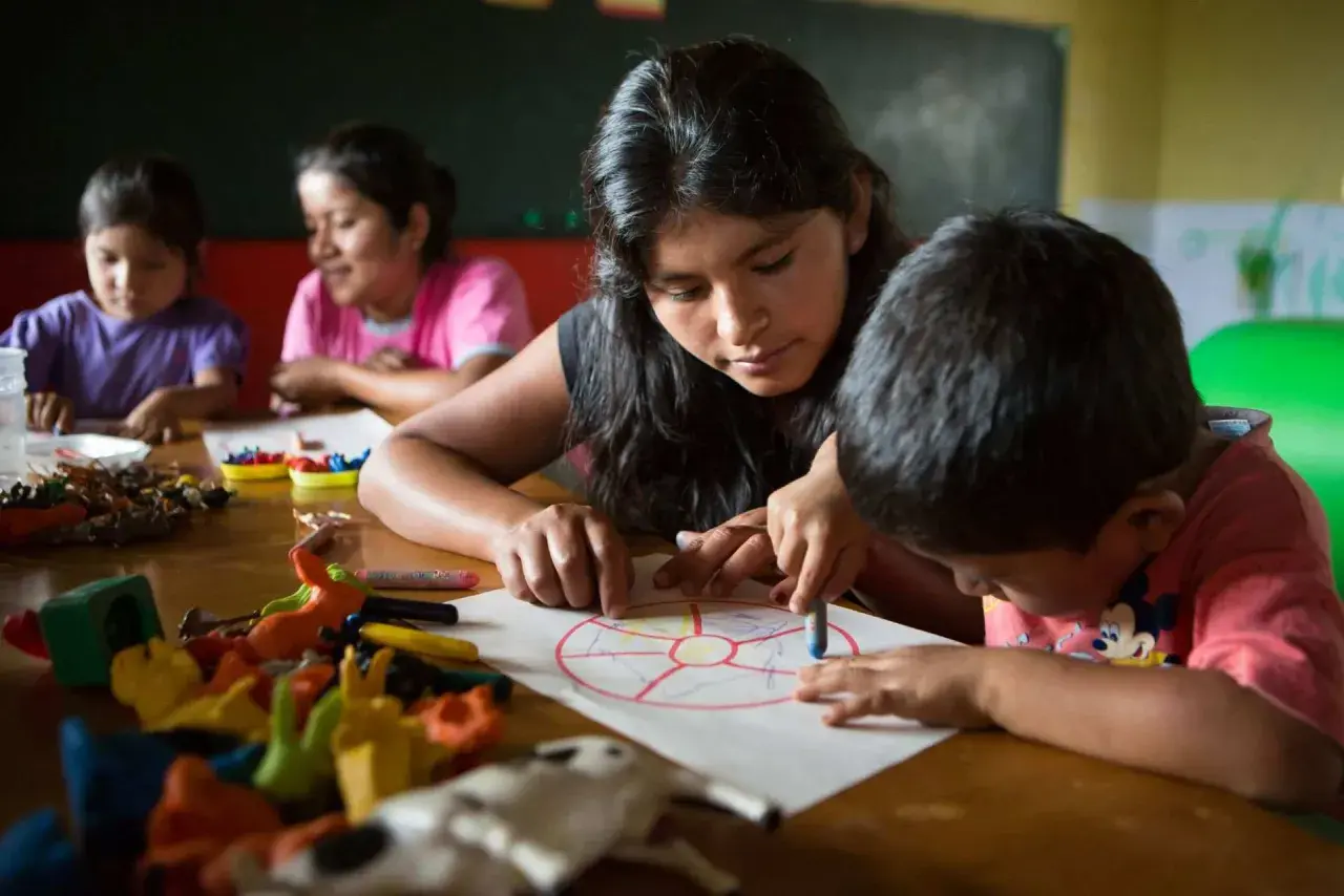 Joven guía a niños en actividad de educación en valores infantil, coloreando un círculo dividido en secciones.
