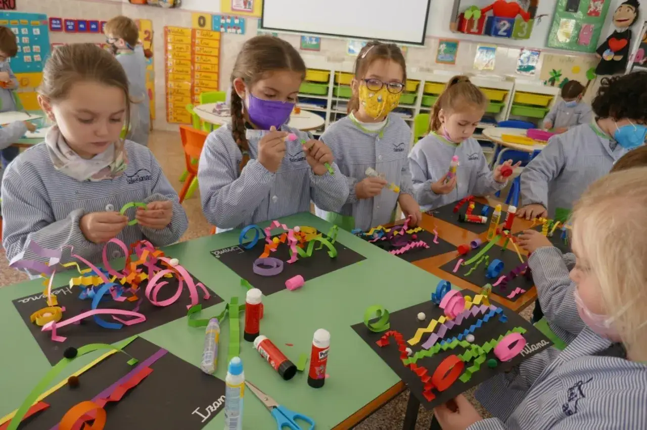 Ni&ntilde;os concentrados en un proyecto de trabajo por proyectos infantil, creando coloridas manualidades con tiras de papel y pegamento.