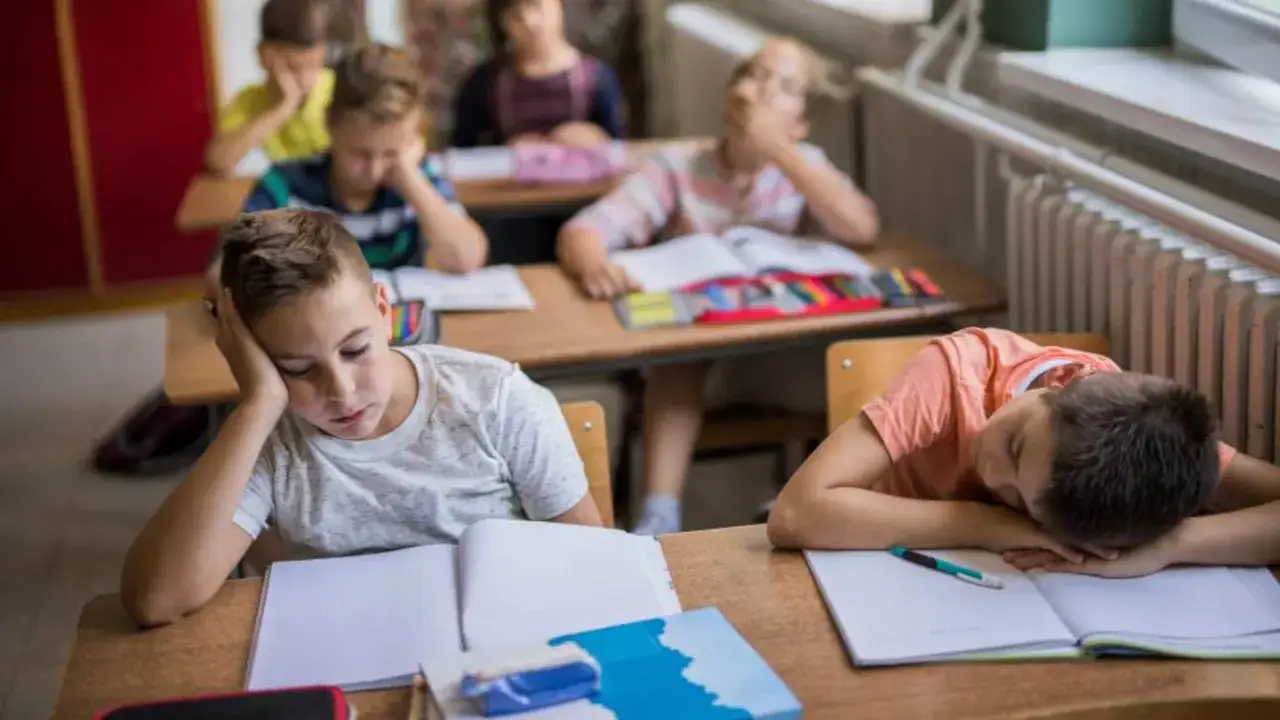Niños aburridos en un aula, reflejo de la educación tradicional. Uno apoya la cabeza en la mano, otro duerme sobre su libro.