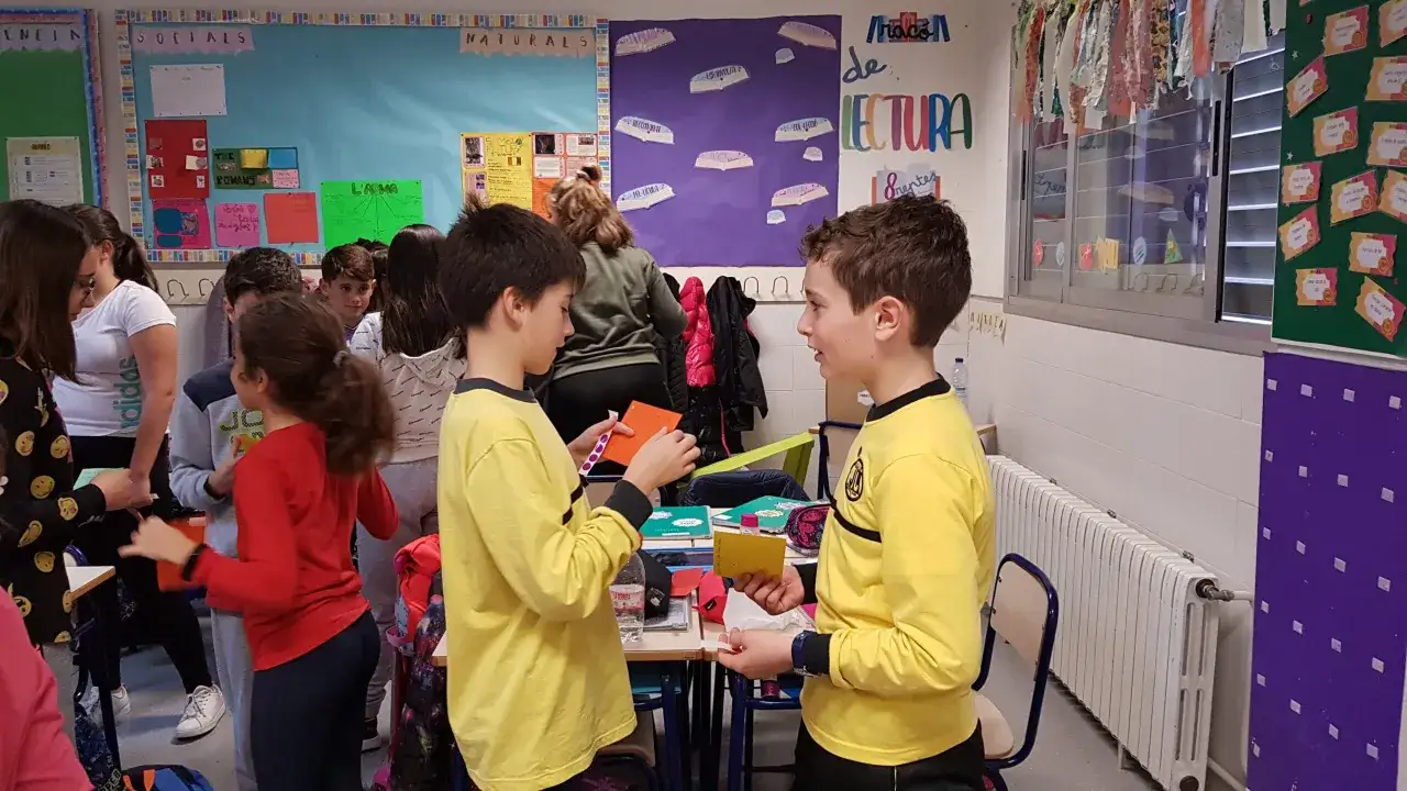 Ni&ntilde;os interactuando en clase, mostrando las ventajas del aprendizaje cooperativo al compartir materiales y colaborar en actividades.