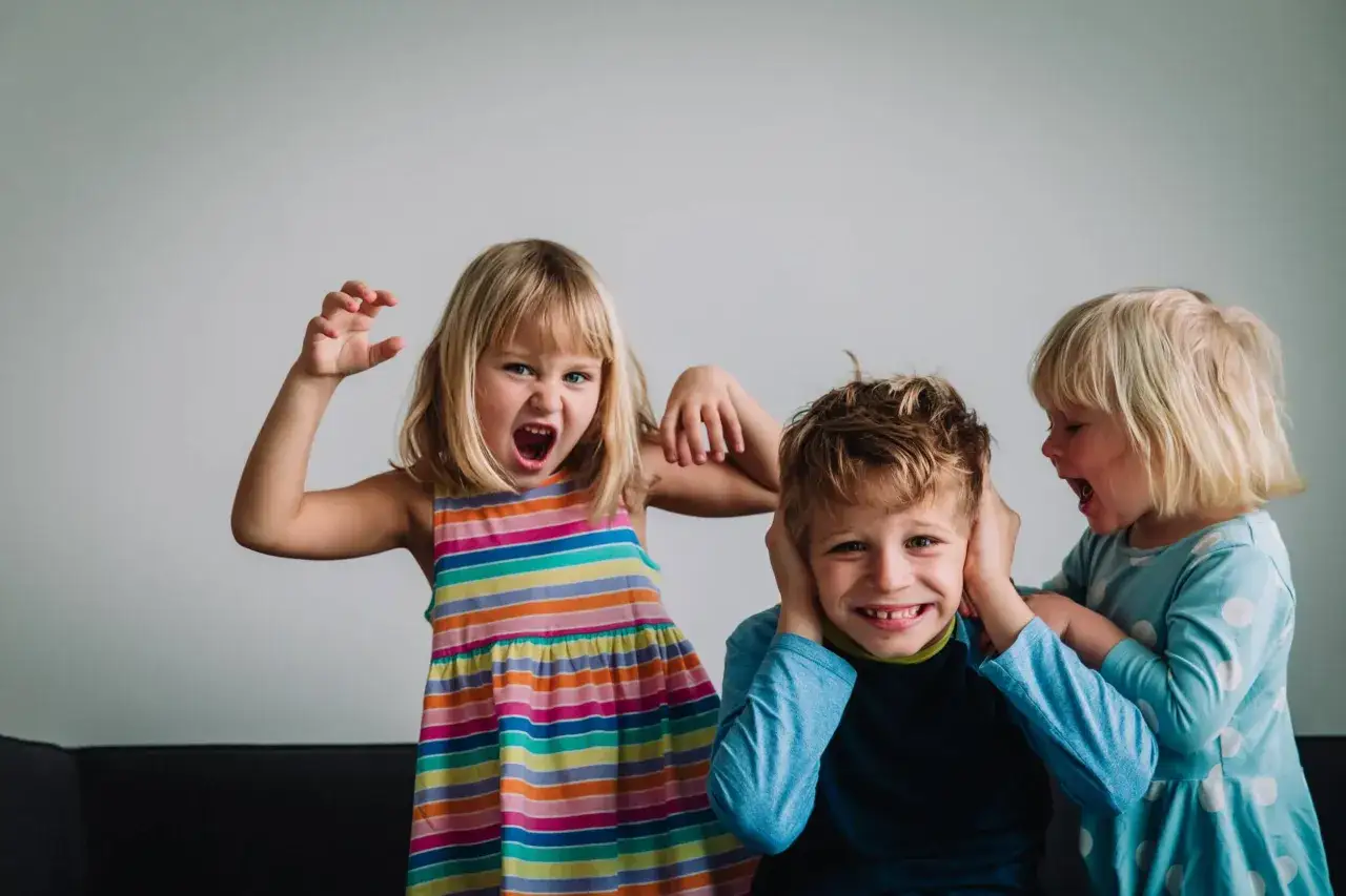 Niños expresando emociones fuertes. La niña de rayas grita, mientras otra le tapa los oídos a un niño. Un ejemplo de retos en la inteligencia emocional infantil.