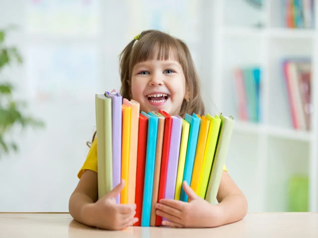 Ni&ntilde;a feliz abraza libros de colores, lista para descubrir m&eacute;todos para aprender a leer.