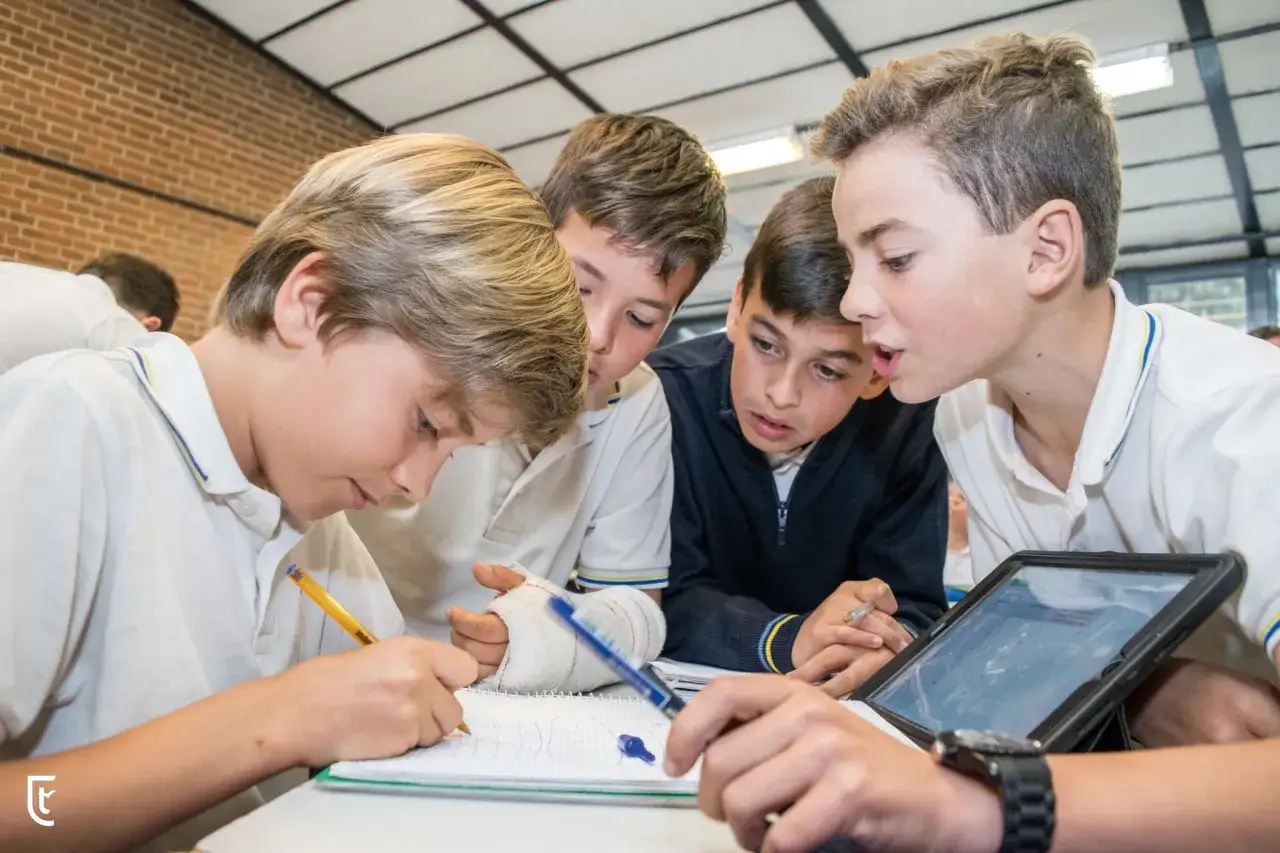 Chicos colaboran en un proyecto, explorando cuáles son las metodologías activas. Uno escribe, otro consulta una tablet, todos concentrados.