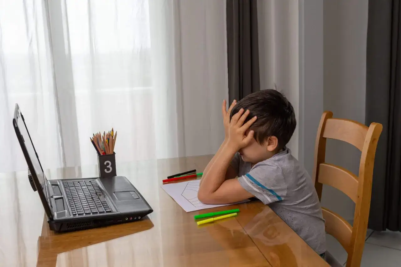 Ni&ntilde;o frustrado con las manos en la cara frente a una laptop. &iquest;Qu&eacute; hago si mi hijo no quiere estudiar?