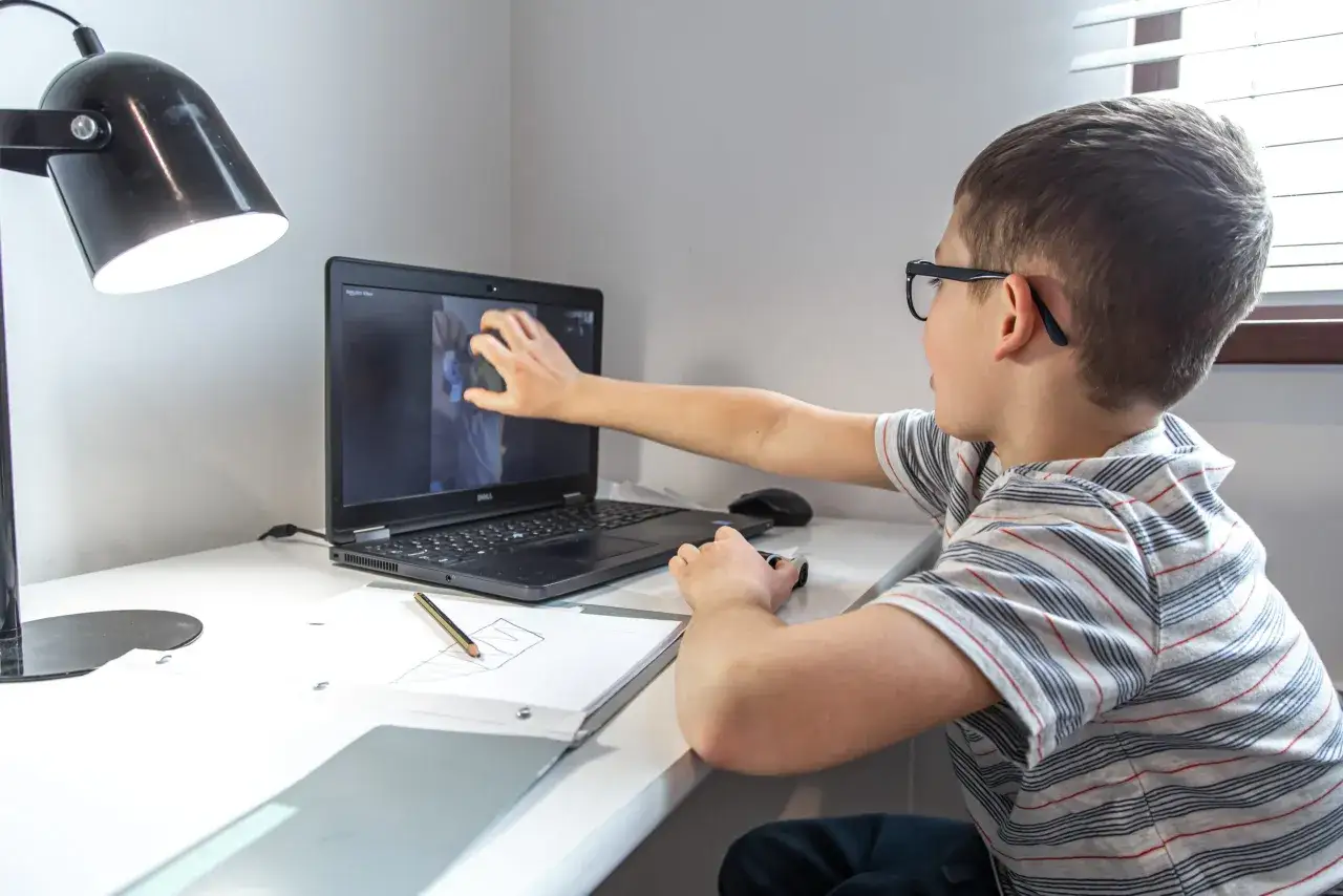 Niño con gafas interactúa con videos educativos para niños de 10 a 12 años en su portátil.