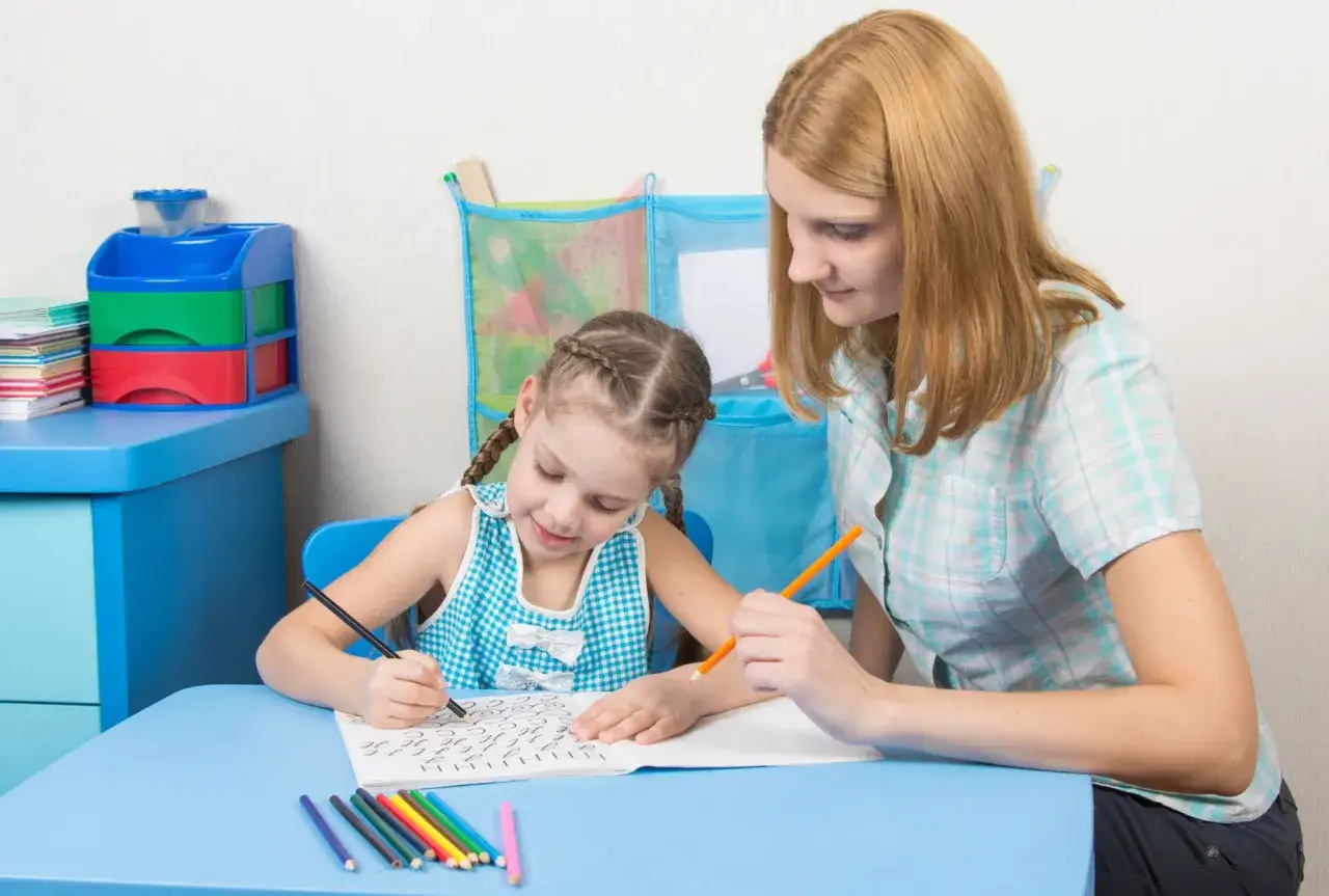 Niña practica ejercicios para aprender a escribir con ayuda de su maestra.