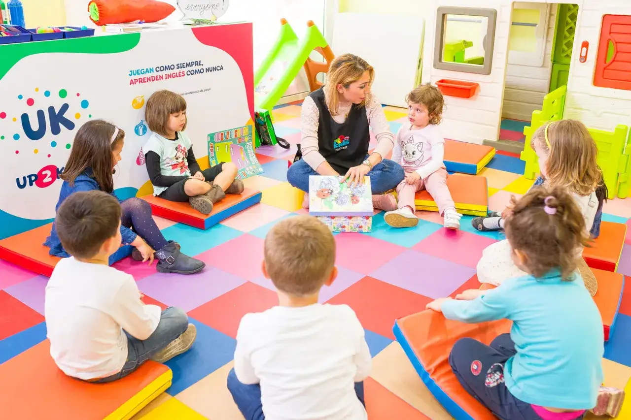 Ni&ntilde;os sentados en c&iacute;rculo, aprendiendo ingl&eacute;s con una maestra. Un ejemplo de gamificaci&oacute;n educativa, donde el juego es la clave.