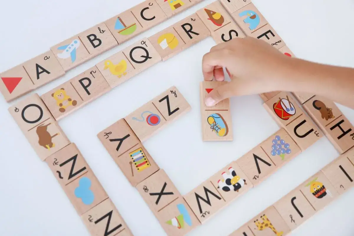 Un niño aprende a leer jugando con fichas de madera del abecedario. Cada ficha tiene una letra y un dibujo.