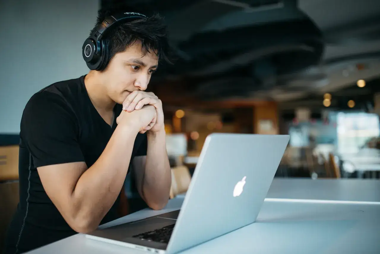 Joven con auriculares y manos juntas frente a una laptop, aprendiendo c&oacute;mo concentrarse en su tarea.
